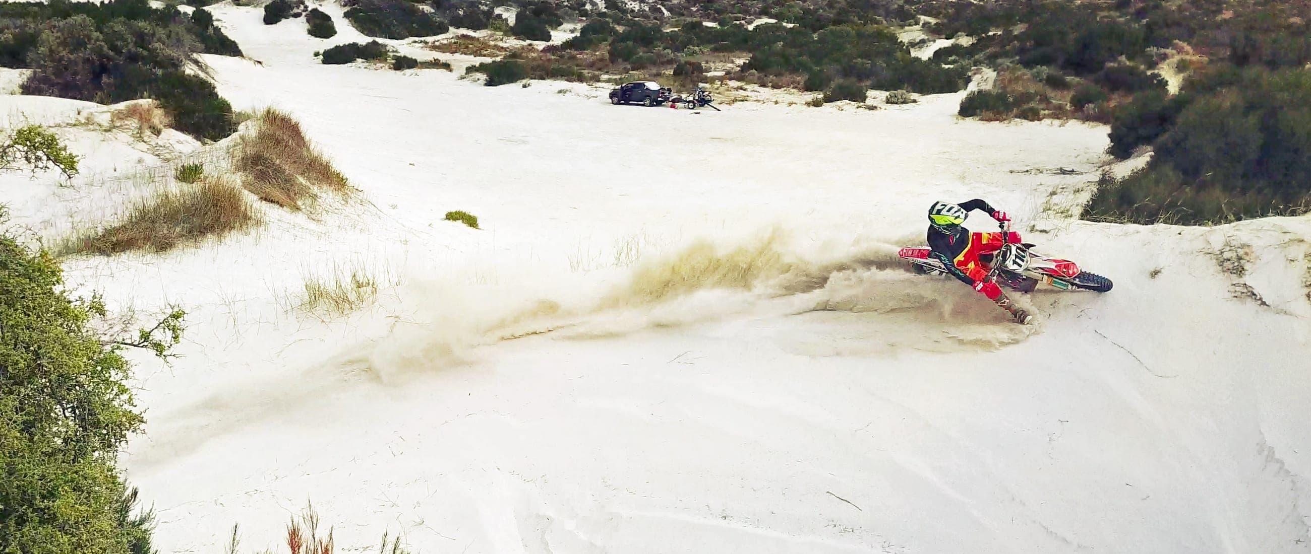 A dirt bike roosting sand across white coastal dunes.