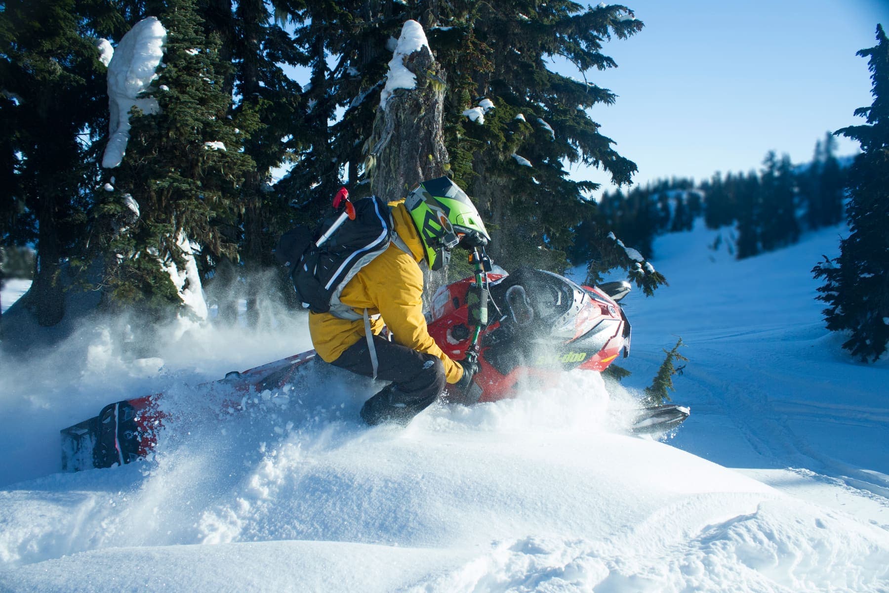 A snowmobile throwing snow in deep backcountry against low sun.